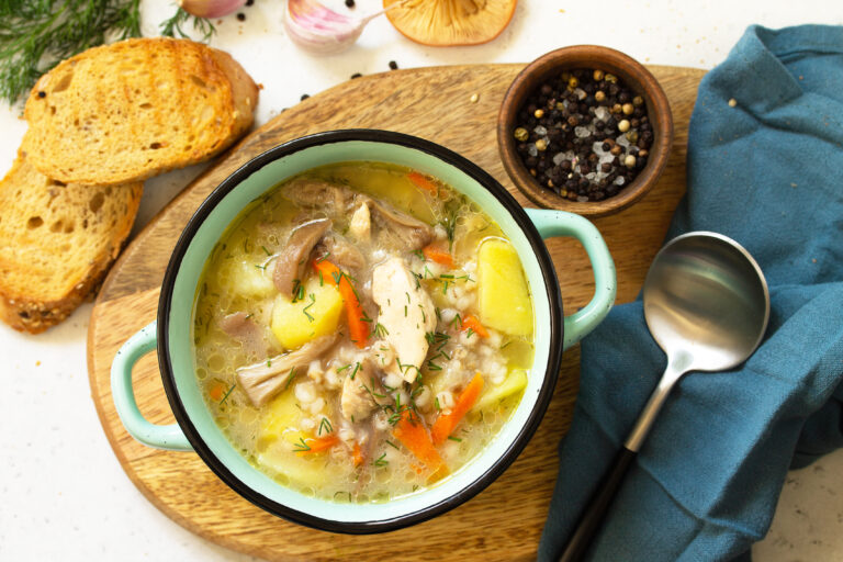 Bowl of traditional hen soup with vegetables, fresh herbs, and golden broth on a wooden surface