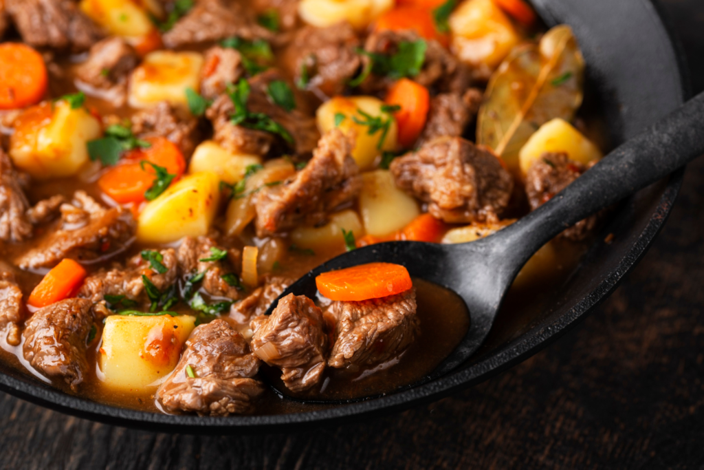 Close-up of tender braised beef cheeks served over creamy mashed potatoes, topped with rich red wine sauce and fresh herbs, on a rustic ceramic plate.