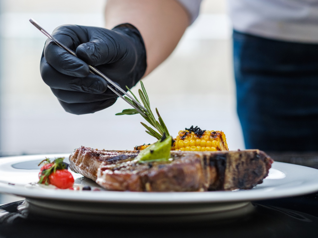 Bone-in ribeye steak sizzling in a cast iron skillet, with a golden crust forming, surrounded by garlic cloves, rosemary, and melted butter.