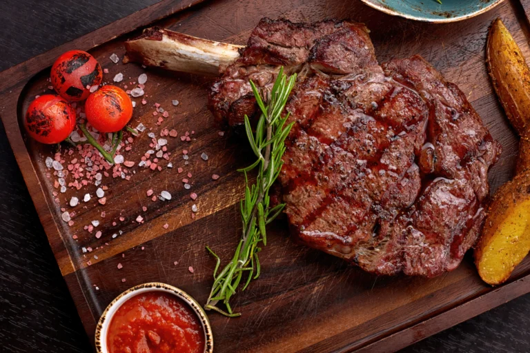Perfectly seared bone-in ribeye steak with a charred crust, resting on a wooden cutting board, garnished with fresh rosemary and sea salt.